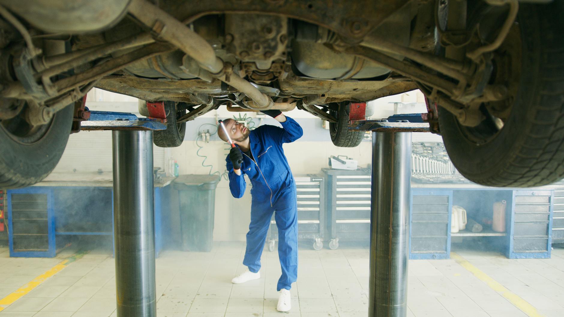 Mechanik w niebieskim kombinezonie sprawdza samochód na podnośniku w warsztacie