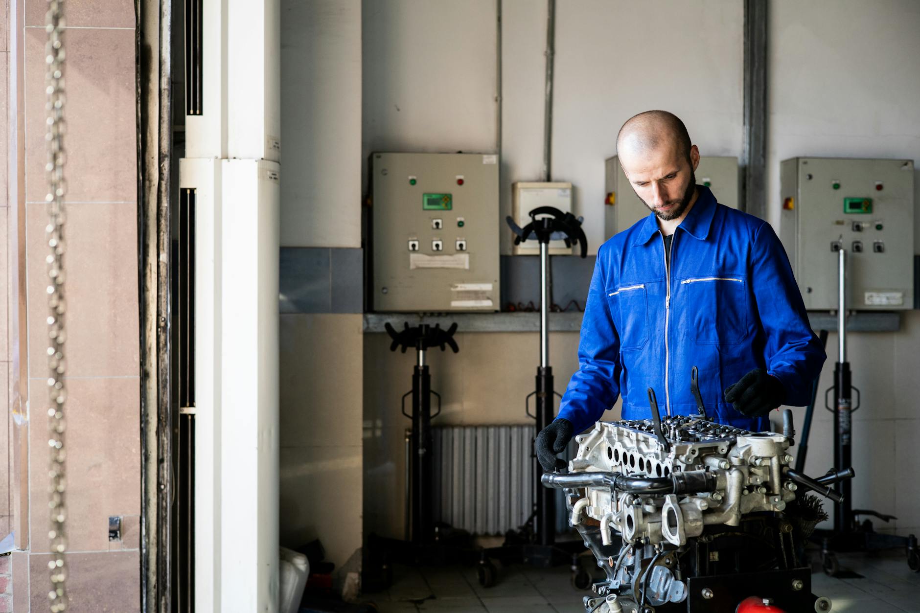 Mechanik w niebieskim kombinezonie sprawdza silnik w warsztacie serwisowym