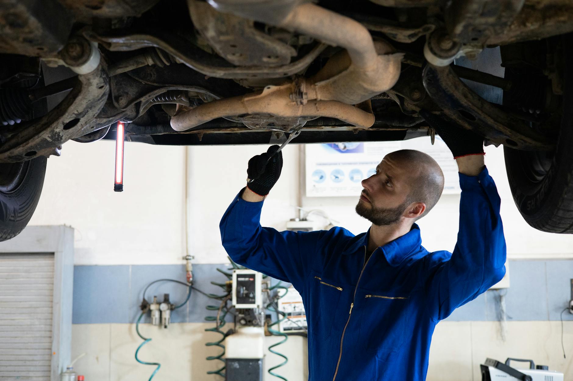 Mechanik w niebieskim kombinezonie sprawdza układ wydechowy samochodu