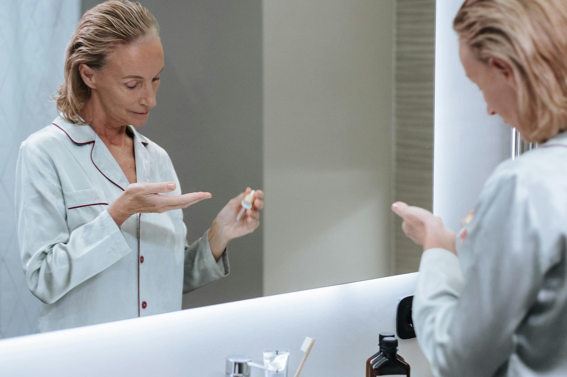 Dojrzała kobieta nakłada serum na twarz przed lustrem w łazience
