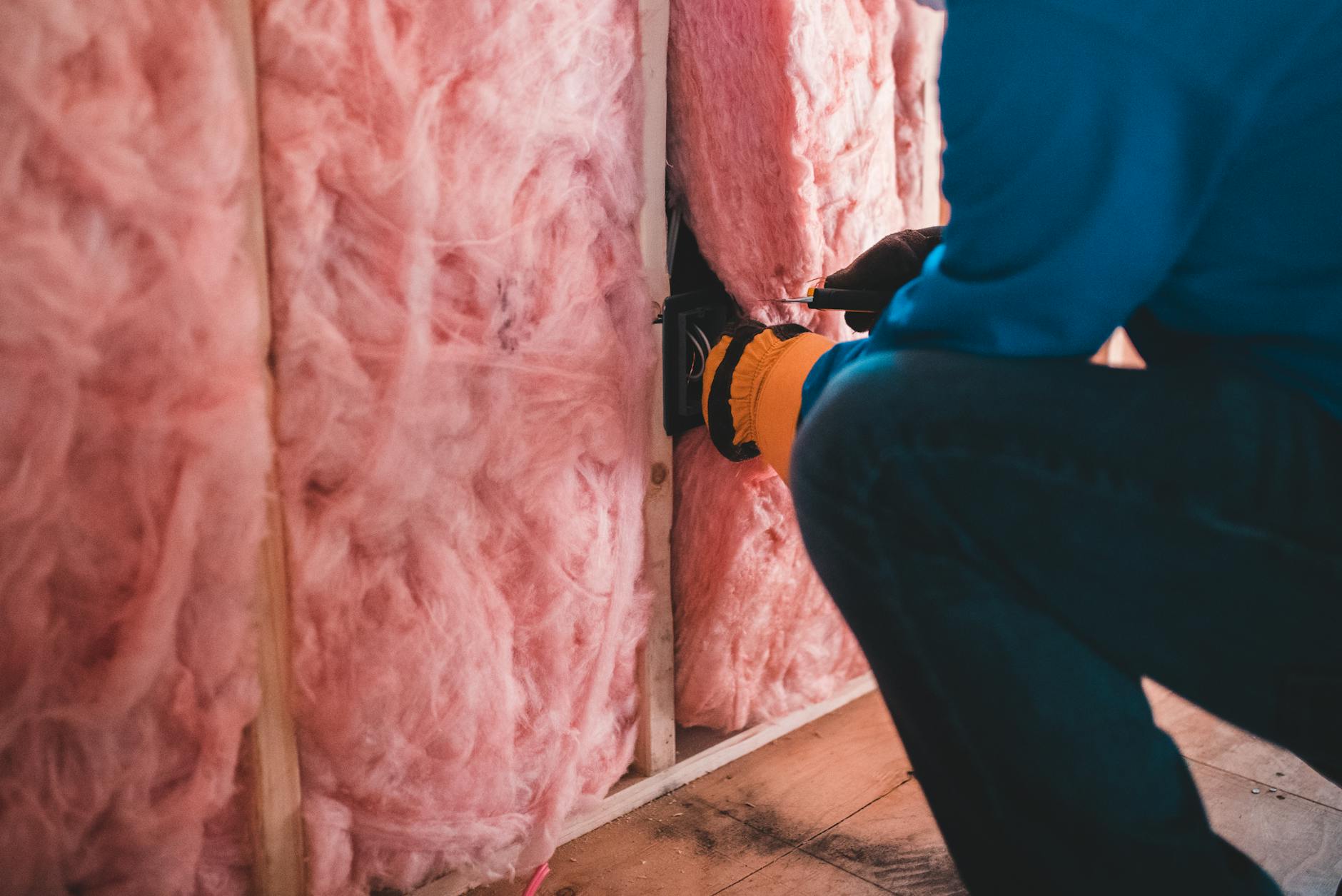Pracownik montuje różową wełnę mineralną podczas ocieplania domu