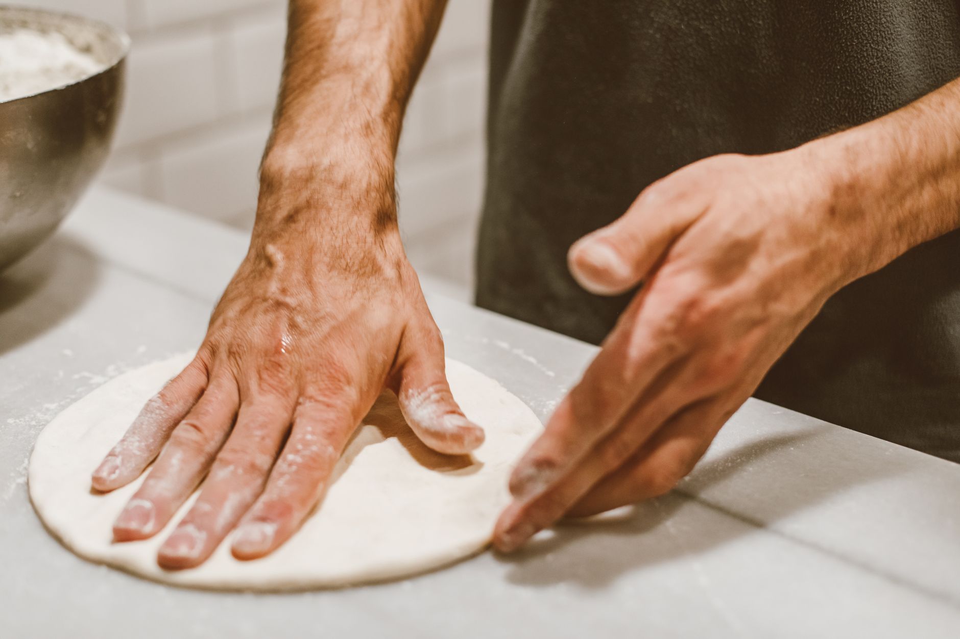 Dłonie formujące ciasto na pizzę w kuchni domowej