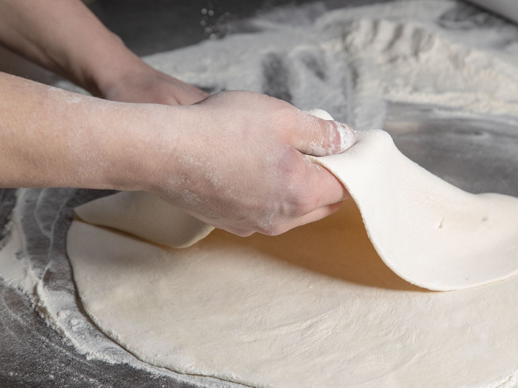 Dłonie wyrabiające włoskie ciasto na pizzę na oprószonym mąką blacie